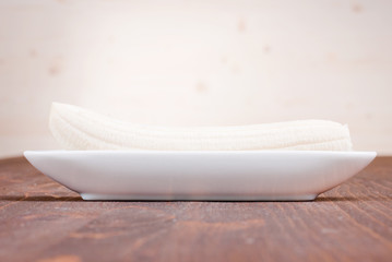 Canvas Print - one peeled banana on a plate on a brown table side view