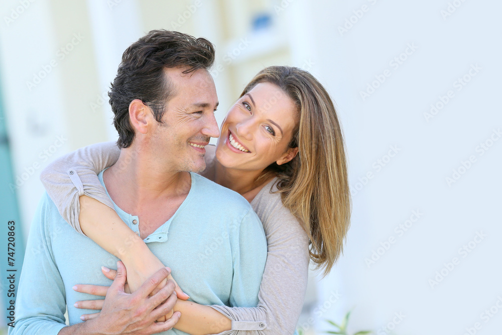 Middle-aged couple embracing in front of house - obrazy, fototapety, plakaty 