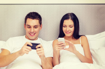 Canvas Print - smiling couple in bed with smartphones