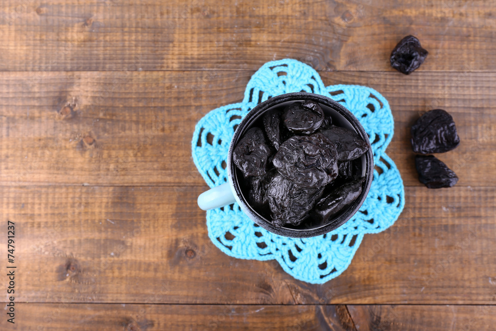 Cup filled with prunes on blue lace doily, on wooden background