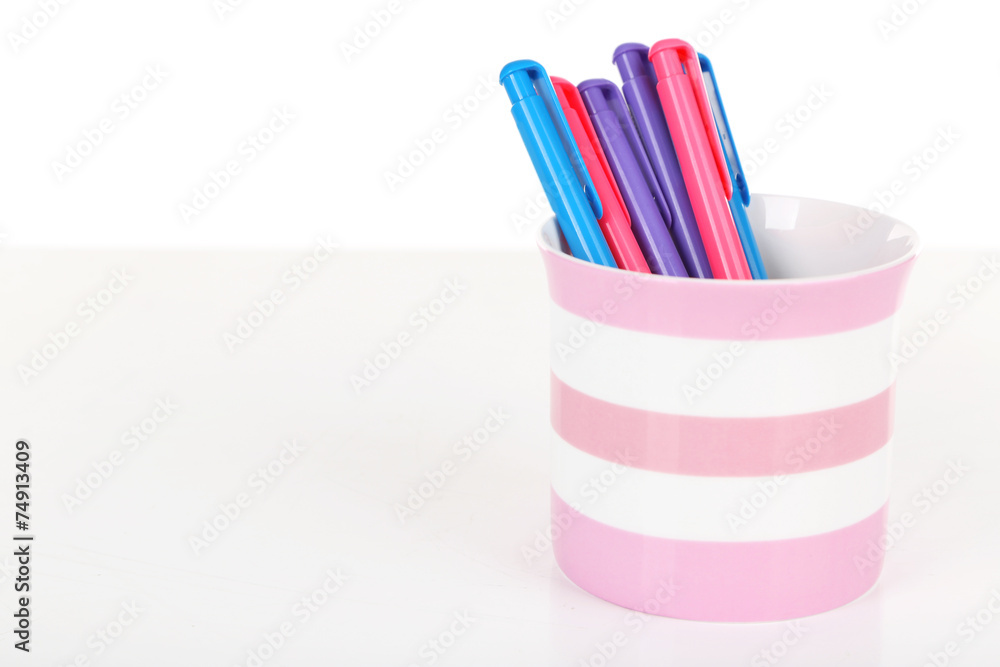 Colorful pens in striped plastic cup isolated