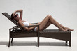 Beautiful tan female model sunbathing in bikini on chaise-longue