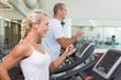 © WavebreakMediaMicro - Side view of couple running on treadmills at gym