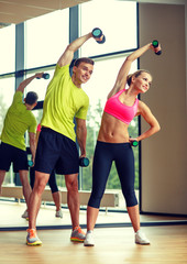 Wall Mural - smiling man and woman with dumbbells in gym