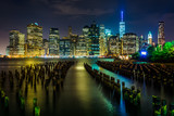 Fototapeta Londyn - Pier pilings and the Manhattan skyline at night, seen from Brook