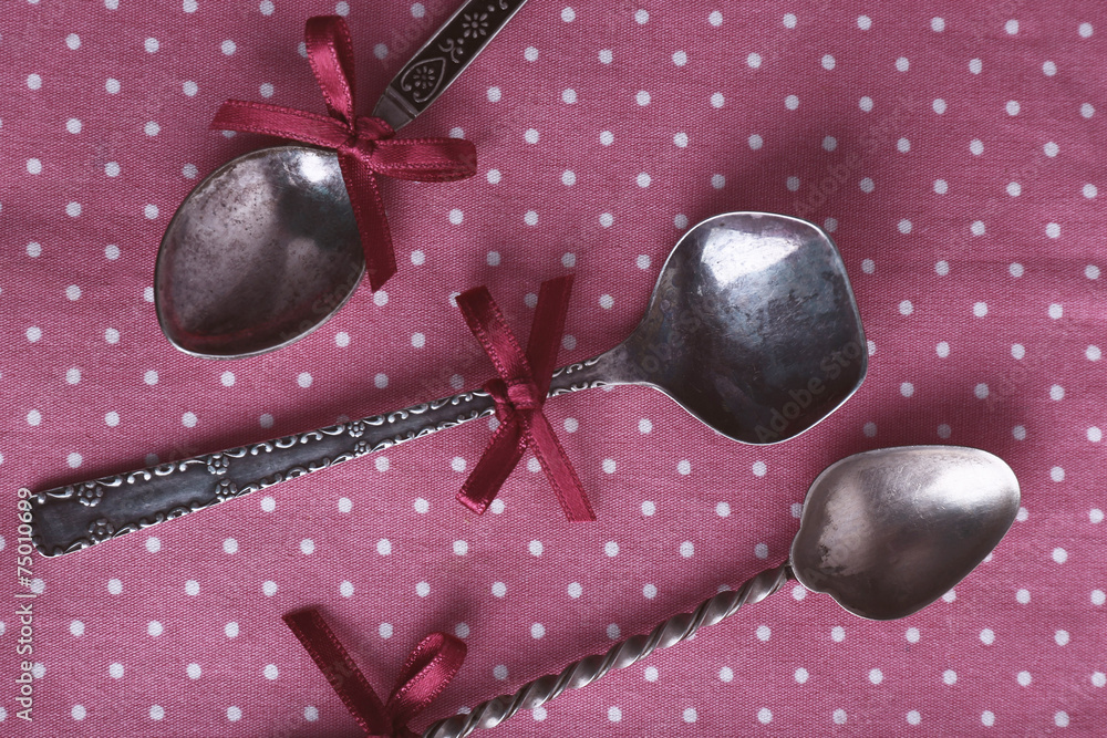 Metal spoons on pink polka dot fabric background