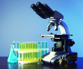 Microscope and test tubes on table, on color background