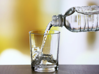 Wall Mural - Pouring water from bottle on  glass on light background