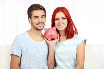 Poster - Loving couple sitting in sofa with piggy bank in room