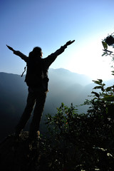 Wall Mural - cheering woman hiker open arms at mountain peak 