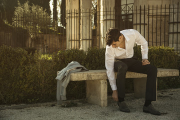 Wall Mural - Handsome young man in European city, sitting on stone bench