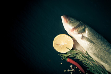 Wall Mural - Fresh fish, lemon, pepper and rosemary on a black background. Ti