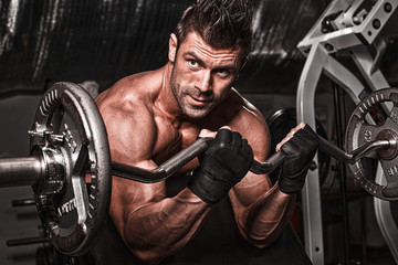 Wall Mural - Closeup of a muscular young man lifting weights on dark backgrou