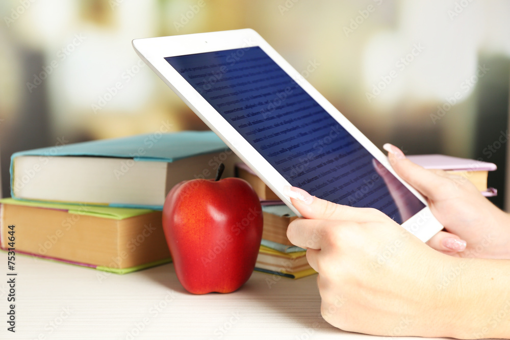 Female hand holding PC tablet near books, close-up. Modern