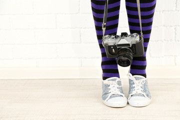 Girl in sneakers with retro photo camera in room