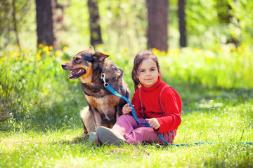 Wall Mural - Happy little girl with big dog sitting on green lawn