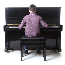 Teenage Boy Sits At Upright Piano In Studio