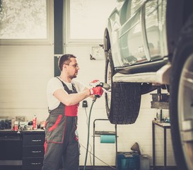 Poster - Serviceman unscrewing wheel in car workshop