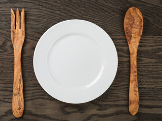 Poster - empty white plate with wood fork and spoon on oak table