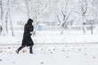 Woman dressed in black coat walking alone during heavy snowstorm