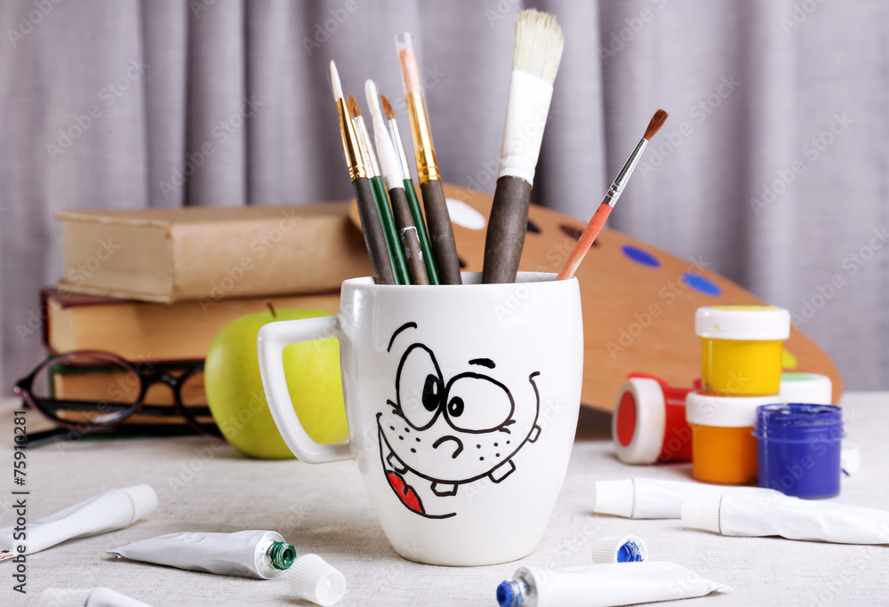 Emotional cup with brushes and paints on wooden table