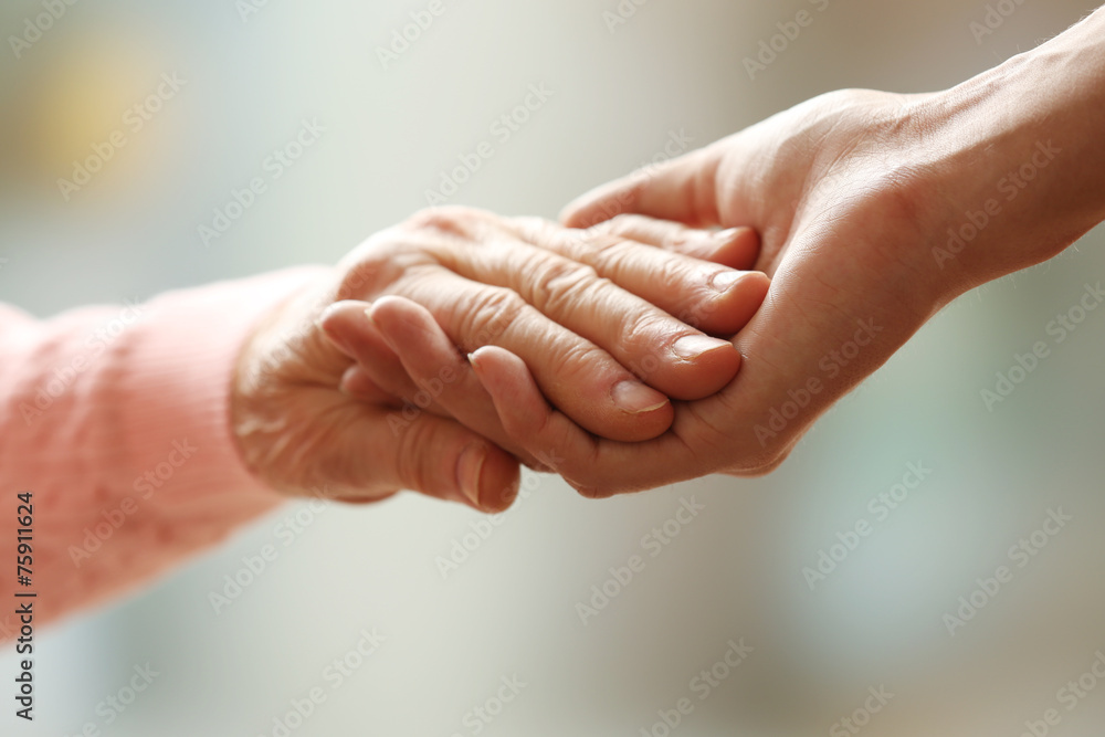 Old and young holding hands on light background, closeup