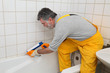 Worker plumber caulking bath tube and tiles with silicone glue