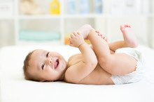Baby Lying On White Bed And Holding Legs