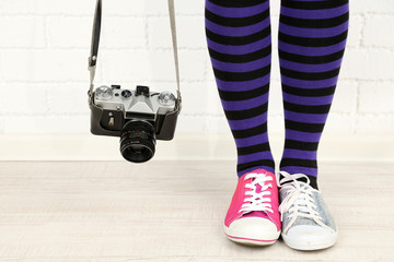 Girl in sneakers with retro photo camera in room