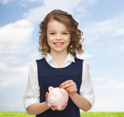 Wall Mural - smiling girl putting coin into piggy bank