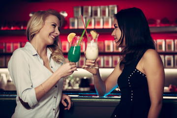 two beautiful women drinking cocktail in a night club and having