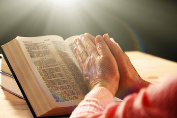 Wall Mural - Hands of old woman with Bible on table and dark background