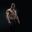 Fit young bodybuilder posing over black background