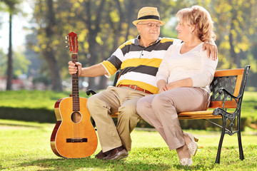 Wall Mural - Mature man sitting with his wife in park and holding guitar