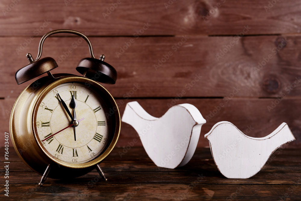 Retro clock with decorative birds on table on wooden background