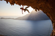 Rock climber climbing along roof in cave at sunset