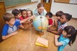 © WavebreakMediaMicro - Cute pupils and teacher in classroom with globe
