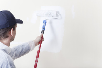 Maler streicht Wand mit Farbrolle weiss