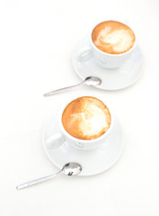 Two white cups of Cappuccino coffee with heart shaped milk foam