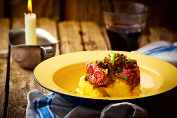 Poster - roast beef and polenta in an iron bowl on a wooden table.