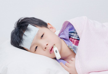 Wall Mural - Little sick boy lying on bed with digital thermometer in mouth