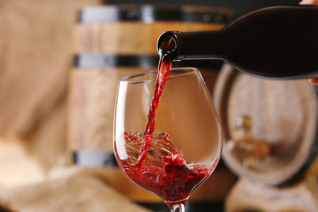 Canvas Print - Pouring red wine from bottle into glass with wooden wine casks