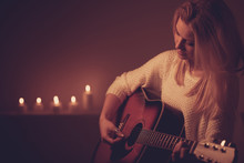 Young Blonde Woman Playing Guitar In Candle Light
