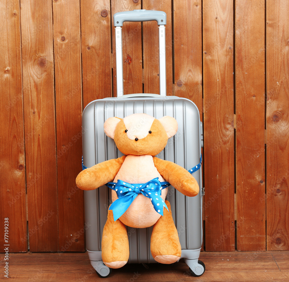 Suitcase with teddy bear on wooden planks background