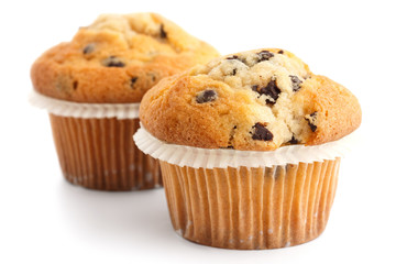 Two light chocolate chip muffins in wax liner on white.