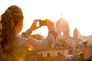 Wall Mural - Young woman taking photo of rome panorama on sunset. rear view