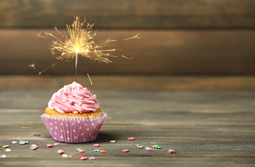 Wall Mural - Cupcake with sparkler on table on wooden background