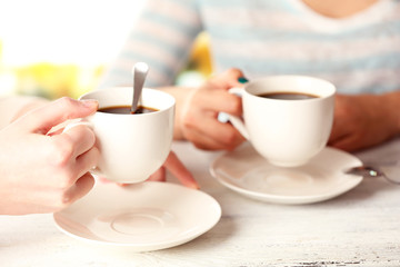 Two women with cups of coffee on bright background