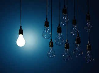 Hanging light bulbs with glowing one isolated on dark blue backg