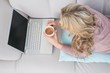 © WavebreakMediaMicro - Blonde lying on couch using laptop while drinking coffee